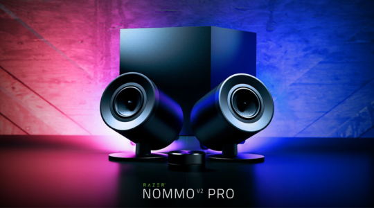 Die beiden Lautsprecher und der passende Subwoofer der Gaming-Soundanlage Razer Nommo V2 Pro vor einem in violett und rosa beleuchteten Hintergrund.